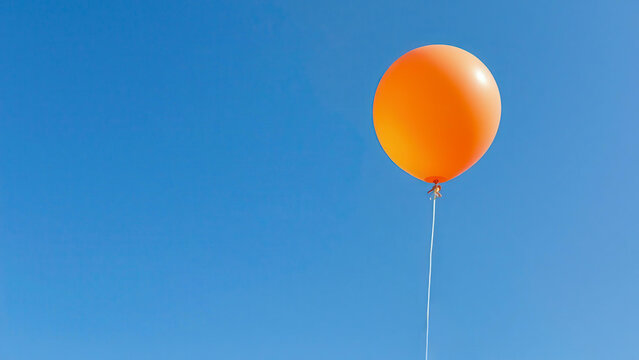 A single orange balloon floats in the clear blue sky. The image symbolizes lightness, freedom and striving upward. Contrasting colors create a bright and minimalistic visual impression. - Powered by Adobe