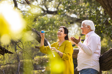 Active senior couple having fun blowing bubbles at park