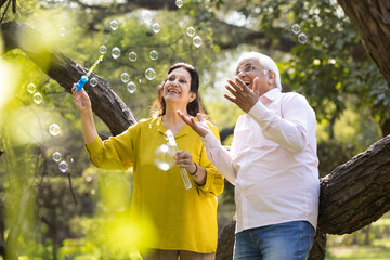Active senior couple having fun blowing bubbles at park