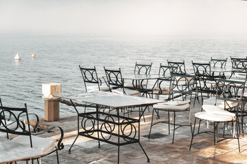 Empty waterfront cafe with wrought iron chairs and misty sea view in Kotor Bay, Montenegro