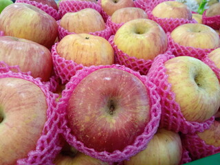 Apples wrapped in foam net are neatly arranged on supermarket shelves for sale