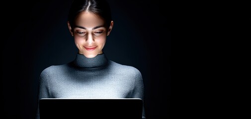 A woman uses a laptop in a dark room, illuminated by the screen, showcasing focus and engagement.