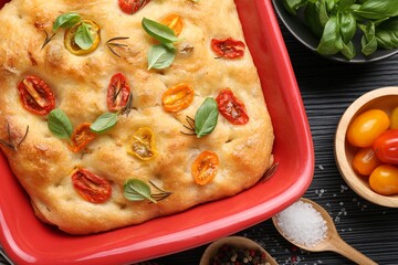 Delicious focaccia with tomatoes and spices in baking dish on table, flat lay