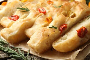 Cut delicious focaccia with tomatoes and rosemary on table, closeup
