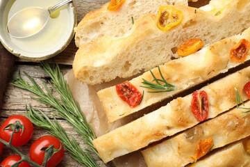 Cut delicious focaccia with tomatoes, spices and oil on wooden table, flat lay