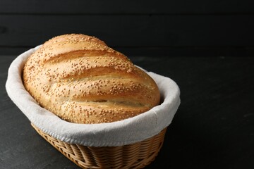 Loaf of bread with sesame seeds in basket on black table, closeup