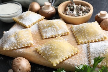 Uncooked ravioli, mushrooms and sauce on black table, closeup