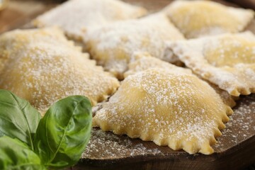 Uncooked ravioli and basil on wooden table, closeup