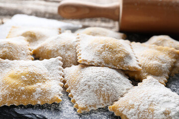 Uncooked ravioli and rolling pin on wooden table, closeup