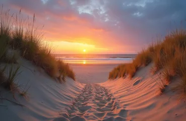 Scenic sunset view over ocean from dunes. Footprints lead to sea shore. Blue sky, orange sun reflection on water, sand dunes. Perfect travel, tourism, vacation concept at beach.