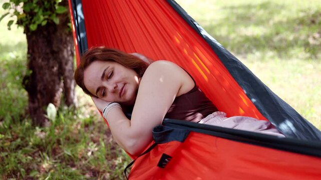 Young calm woman resting in a hammock in a summer garden. Summer vacation concept.