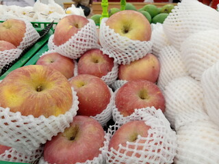 Apples wrapped in foam net are neatly arranged on supermarket shelves for sale