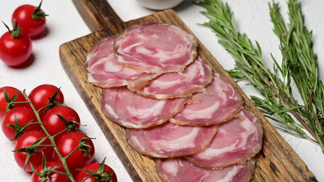 Savor slices of authentic Italian coppa capocollo served with vibrant cherry tomatoes and aromatic herbs on a rustic wooden board