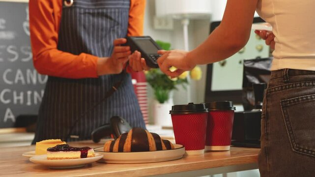 A young Asian female barista in modern cafe assists woman customer ordering latte, fresh coffee beans, dark roast, croissant, completing the purchase with mobile payment at the POS using QR code.