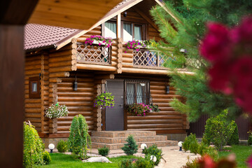Wooden log house with flower-decorated balconies, lush green garden, and elegant landscaping. Peaceful countryside vibe with cozy natural design and outdoor charm.