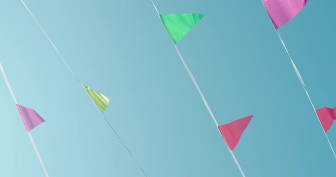 Colorful triangular flags flutter on strings against a clear blue sky, evoking a festive and cheerful outdoor atmosphere.