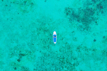 Man paddle boards across calm turquoise sea, tropical beach scene for summer holidays and adventure seekers.