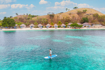 Paddle boarder enjoying crystal clear turquoise sea at tropical beach, ideal summer vacation concept image.
