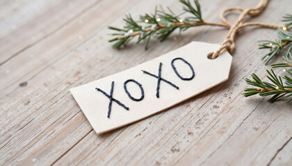 Gift tag with handwritten "XOXO" and evergreen branches on wood  