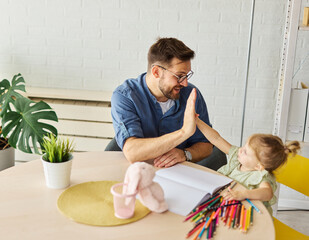 Portrait of a little girl and father or teacher coloring a book in classroom or at home. Education and development concepts