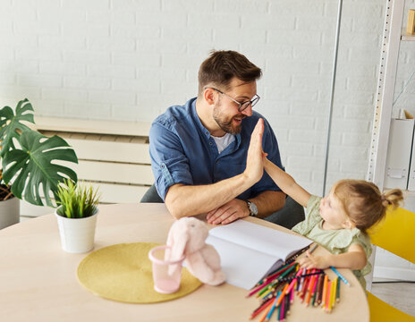 Portrait of a little girl and father or teacher coloring a book in classroom or at home. Education and development concepts