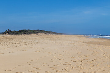 Lake Tyers Beach, Victoria, Australia. Golden sand with scattered footprints, coastal scrubland, ocean waves and blue sky. Quiet Australian beach travel destination in a natural, windswept setting.