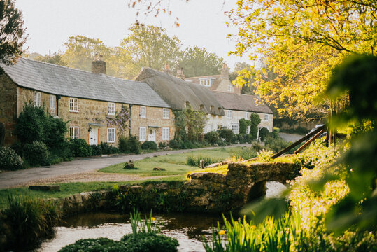 A small town with a bridge over a river and houses on either side. The houses are old and made of stone. The houses are surrounded by trees and bushes