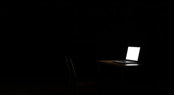 Laptop illuminated on a dark table in a minimalistic room  