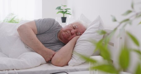 Tranquil senior man sleeping or napping in bed during the early morning hours at home. He enjoying a peaceful slumber, dreaming in the comfort of bedroom as part of restful routine. - Powered by Adobe