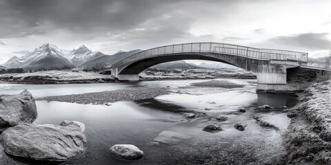 Panoramic photograph of an epic, beautiful, modern bridge across a river, with mountains in the background, during winter.