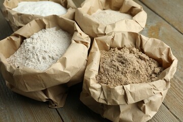 Different types of flour in paper bags on wooden table, closeup