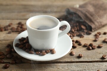 Aromatic coffee in cup and beans on wooden table, closeup