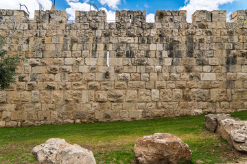 Fragment of a fortress wall of the old city of Jerusalem with a blue cloudy sky and stones on green...