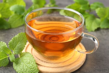Aromatic lemon balm tea in glass cup and fresh leaves on gray table, closeup