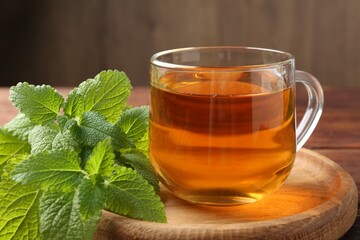 Aromatic lemon balm tea in glass cup and fresh leaves on table, closeup