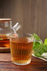 Aromatic lemon balm tea in glass cup, teapot and fresh leaves on wooden table