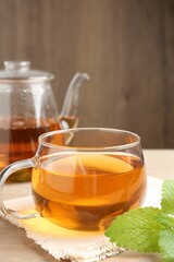 Aromatic lemon balm tea in glass cup, teapot and fresh leaves on table, closeup
