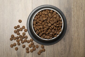 Dry pet food in feeding bowl on wooden background, top view