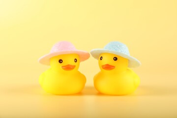Cute rubber ducks in hats on yellow background
