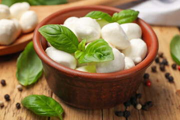 Mozzarella cheese balls with basil and peppercorns on wooden table, closeup