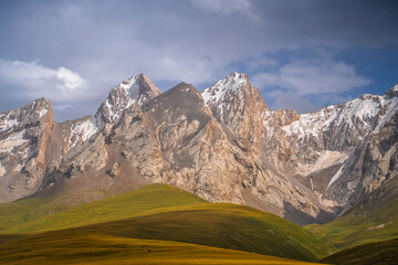 Imposing mountain peaks with snow dusting their summits rise above undulating green and golden...