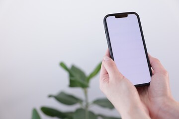 Woman holding smartphone with blank screen on blurred background, closeup. Mockup for design