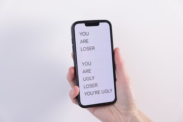 Cyber bullying. Woman holding smartphone with insults on light background, closeup