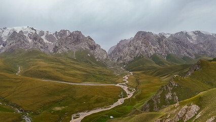 An aerial view of a wide mountain valley with a winding river, flanked by rugged snow-capped peaks...