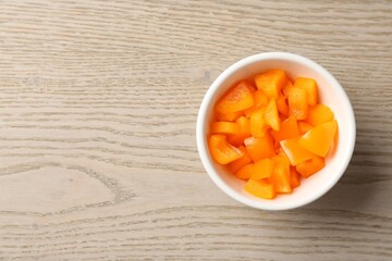 Pieces of fresh orange bell pepper in bowl on wooden table, top view. Space for text