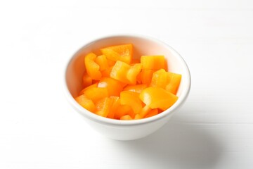Pieces of fresh orange bell pepper in bowl on white wooden table, closeup