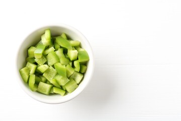 Pieces of fresh green bell pepper in bowl on white wooden table, top view. Space for text