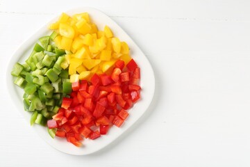 Pieces of fresh colorful bell peppers on white wooden table, top view. Space for text