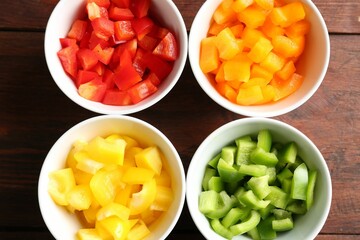 Pieces of fresh colorful bell peppers in bowls on wooden table, flat lay