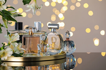 Many different perfume bottles and flowers on mirror surface against light grey background with...